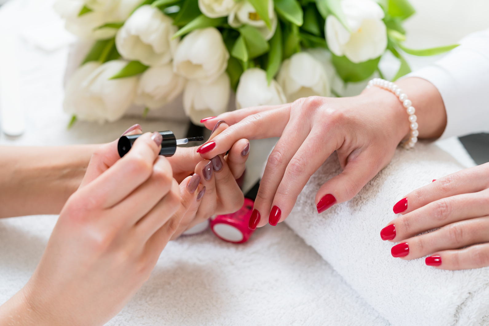 Hands of a Skilled Manicurist Applying Red Nail Polish 